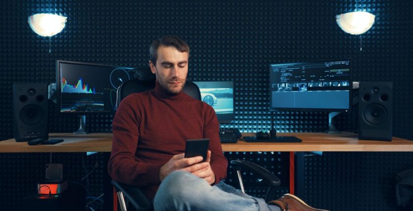 Young man working in the studio using a smartphone and computer.